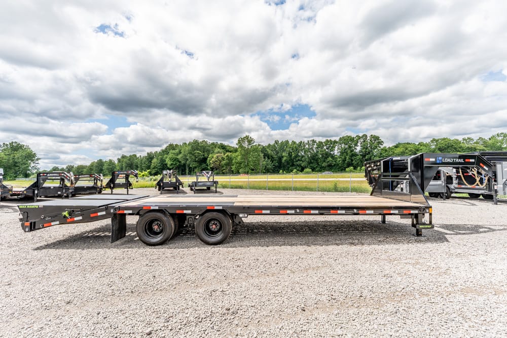Flatbed trailer on a gravel lot with other trailers and a cloudy sky above.
