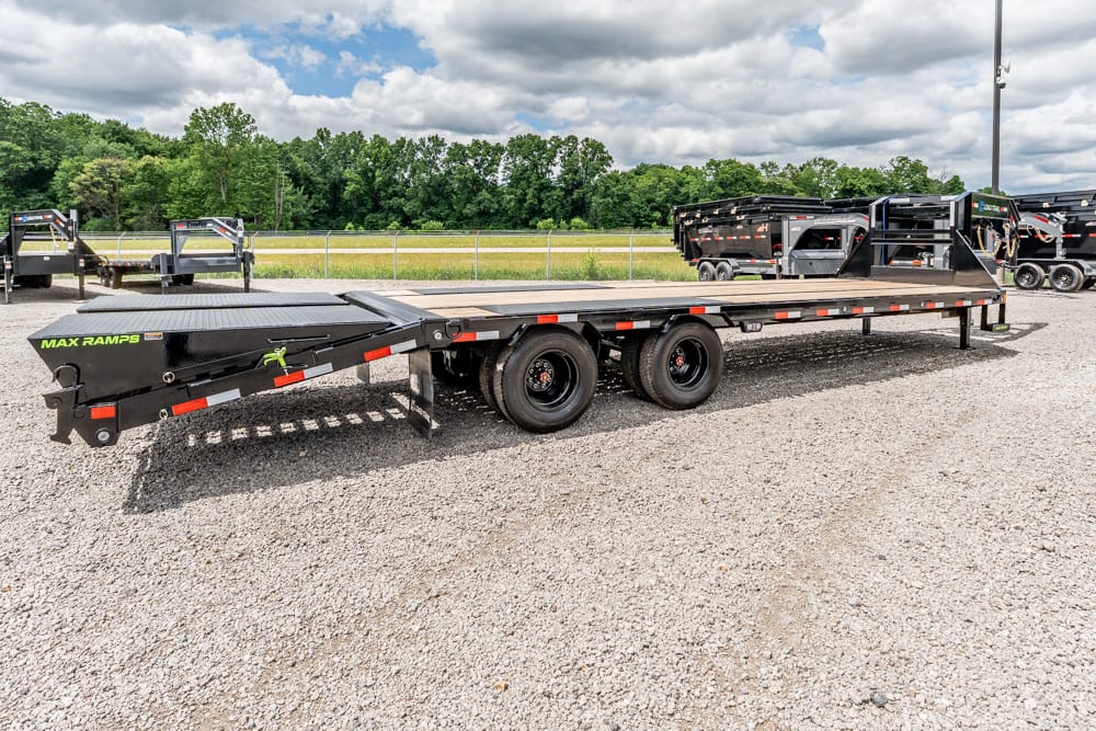 Black Max Ramps lowboy trailer with dual rear axles parked on gravel lot; ramps at front and long flatbed for heavy equipment transport
