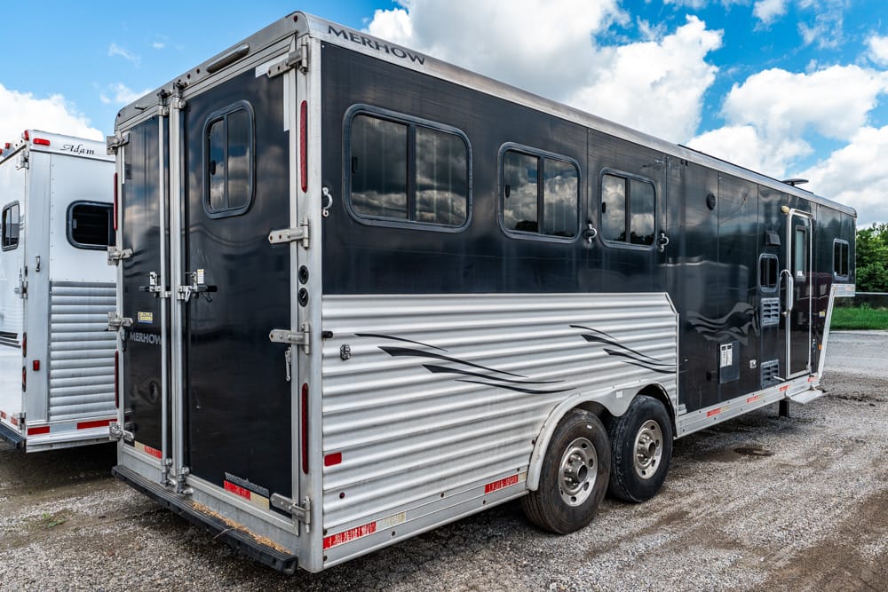 Black horse trailer with silver corrugated lower panels and three windows on the side, parked on gravel yard.