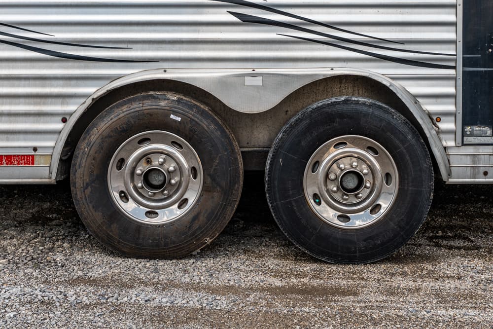 Two large trailer wheels side by side on a silver corrugated trailer with a gravel ground beneath them.