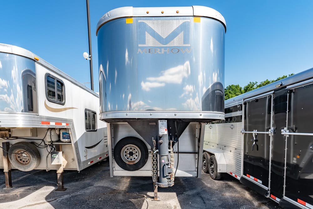 Blue Merhow horse trailer viewed from the front, parked between two other trailers on a sunny day