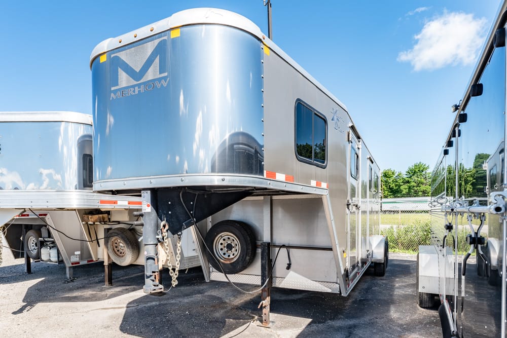 Large blue Merhow gooseneck horse trailer parked in a lot with other trailers nearby, under a clear sky