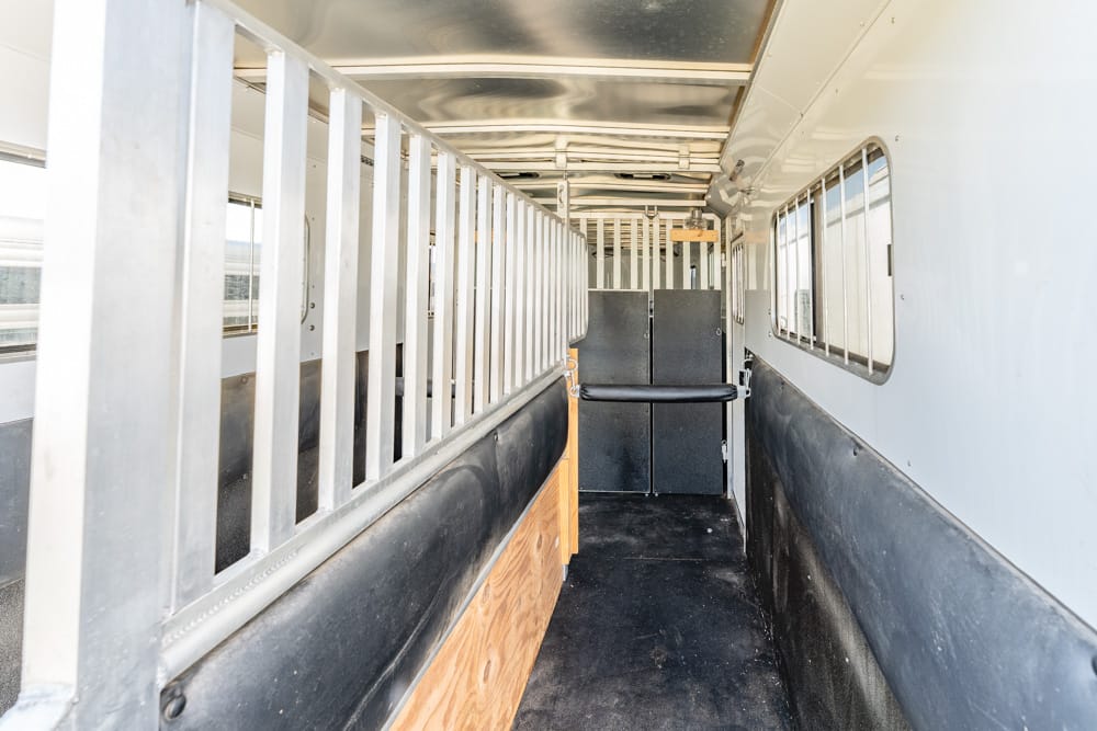 Interior of a horse trailer with metal dividers and a padded side wall at the aisle edge, extending toward the back stall area