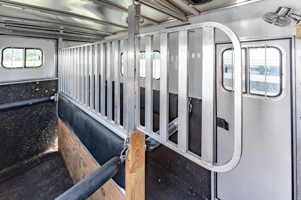 Interior of a horse trailer showing a vertical metal divider forming a stall with side windows and padded wall at the bottom edge.
