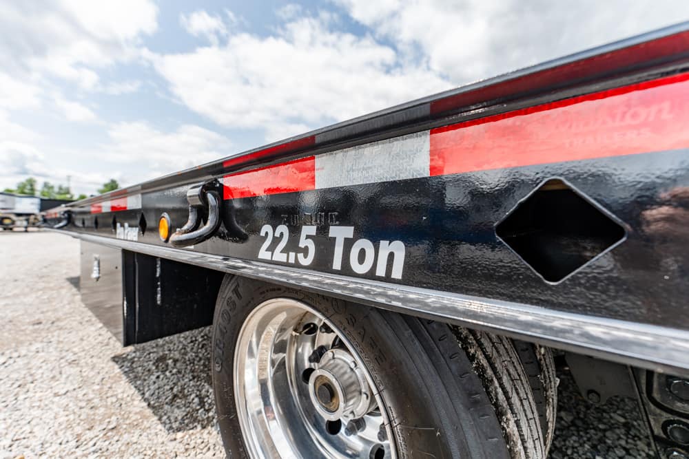 Side view of a black flatbed trailer with a '22.5 Ton' capacity marking and a chrome wheel.