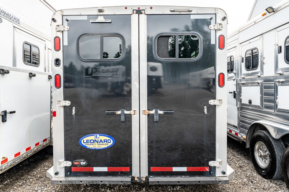Back of a dual-door cargo trailer with a blue Leonard Truck & Trailer logo, red/white reflective strips, on a gravel lot.