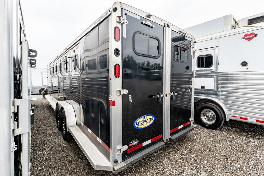 Black enclosed dual‑axle trailer with rear double doors, parked on a gravel lot among other trailers.