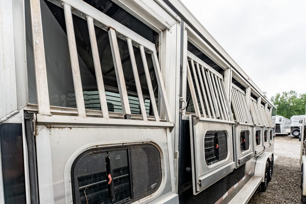 Row of silver livestock trailers with barred windows parked on a gravel lot