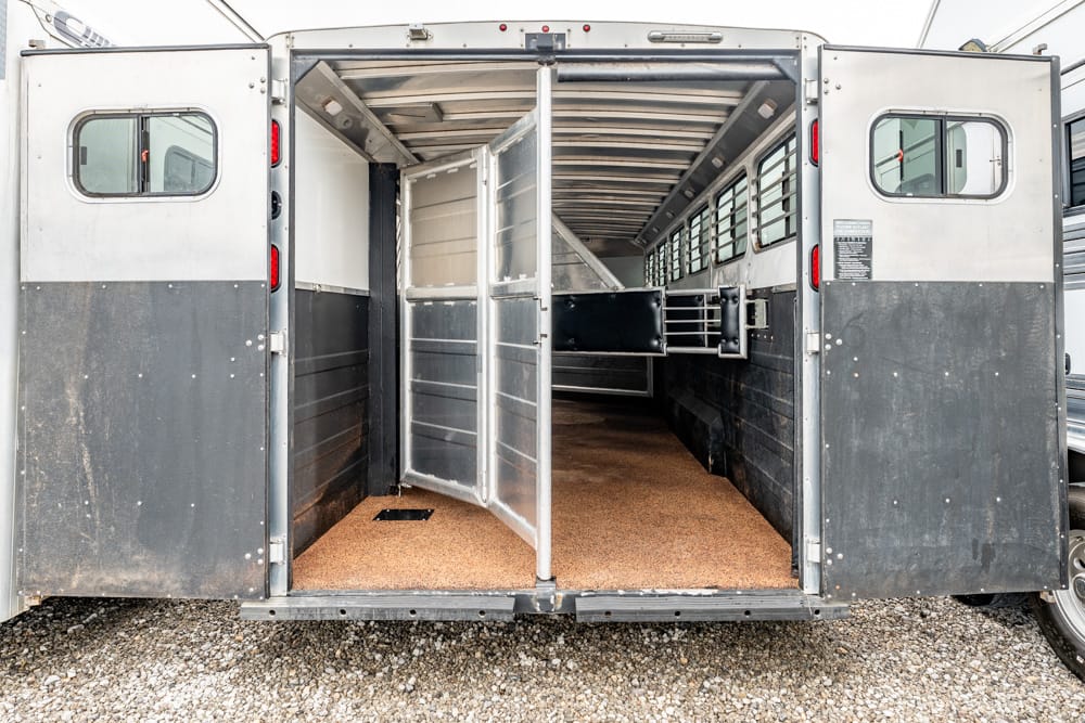 Interior of an empty horse trailer with metal partitions and a cork-like floor.