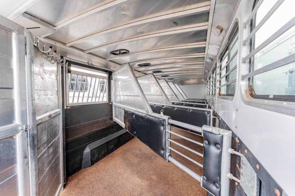 Interior of a metal horse trailer with individual divider stalls and a rubber-padded walkway