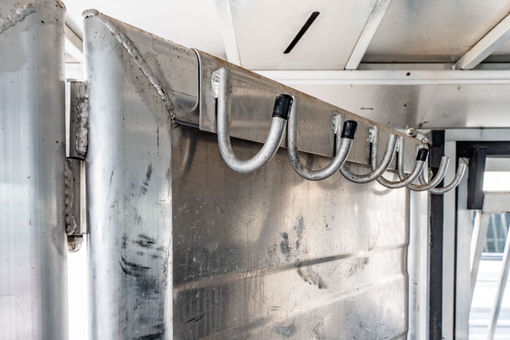 Row of metal hooks attached to a stainless steel panel in a kitchen or workshop setting, used for hanging items.