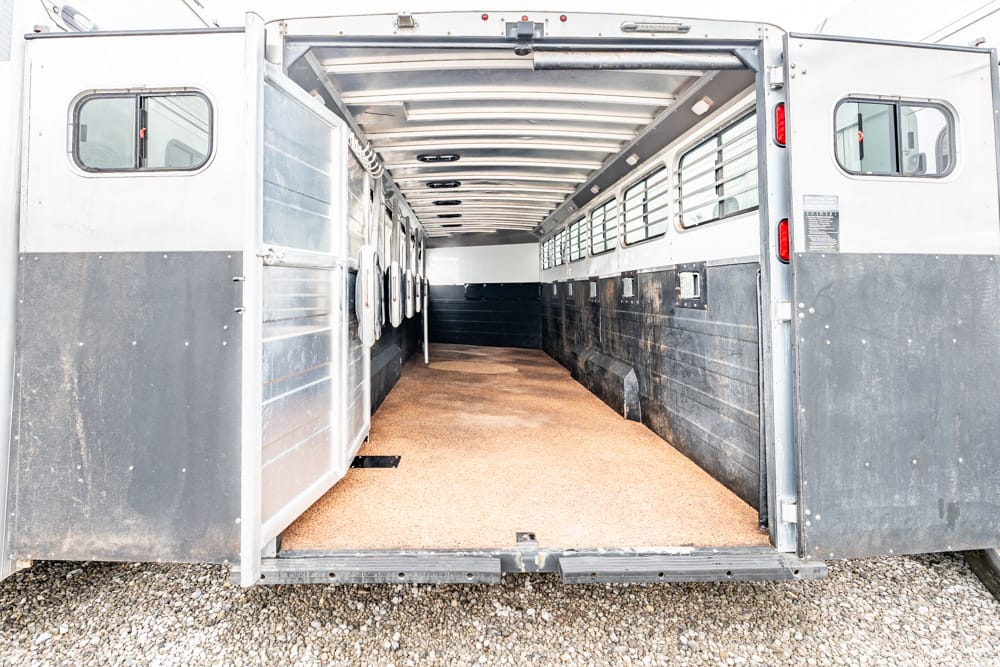 Empty horse trailer interior with divider stalls on the left and windows along the right, brown non-slip floor.