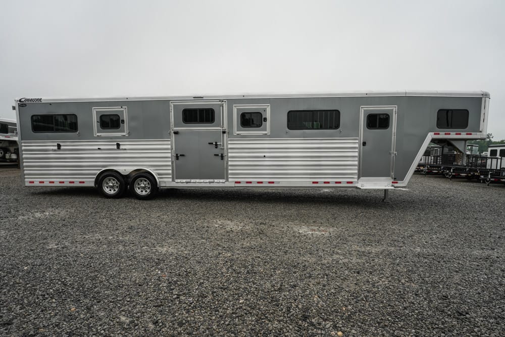 Long silver horse trailer with windows, doors, and tandem axles parked on gravel.