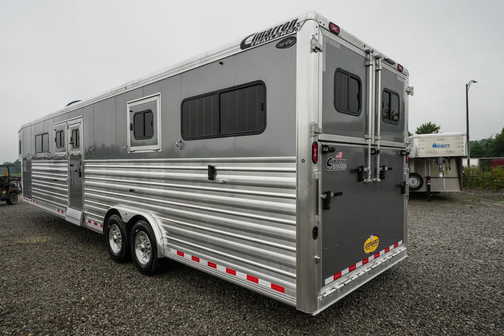 Silver aluminum horse trailer with two axles, ribbed siding, side windows, and rear double doors.