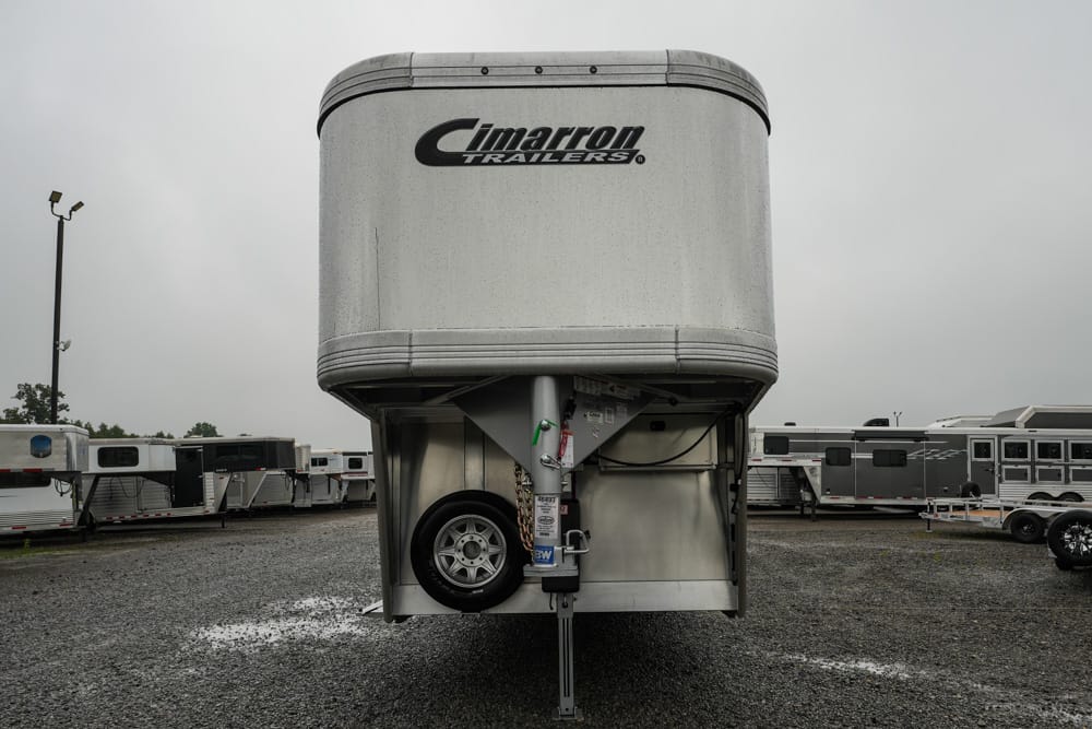 Front view of a Cimarron aluminum gooseneck trailer with spare wheel, parked on a gravel lot.