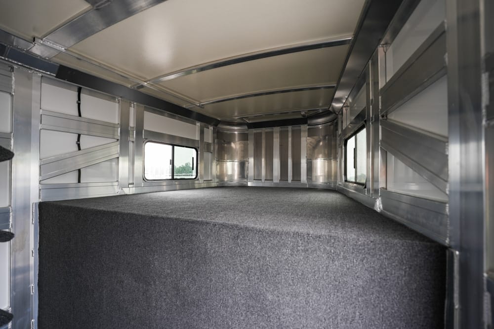 Interior of a metal cargo trailer with a dark carpeted raised platform and small rectangular side windows on each wall.