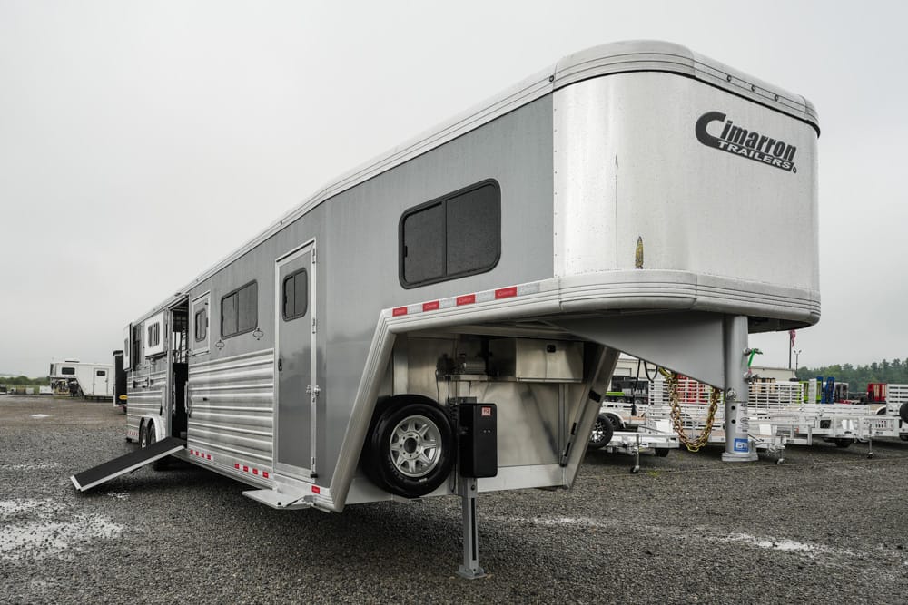 Silver Cimarron gooseneck horse trailer with ramp lowered on a gravel lot at a trailer yard.