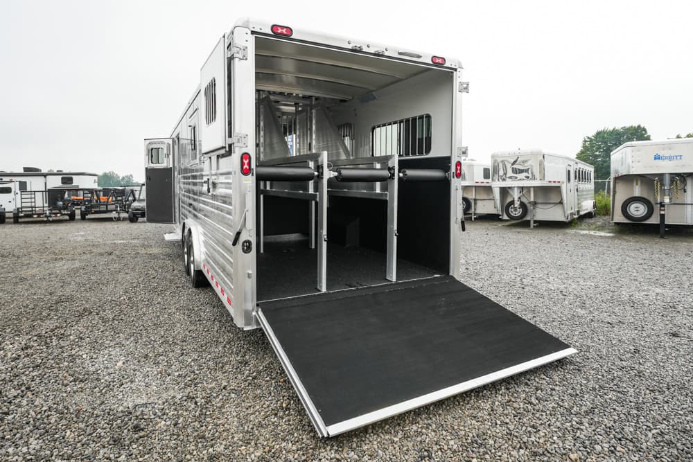 Aluminum horse trailer with the rear ramp lowered, showing two stalls and partition bars inside.