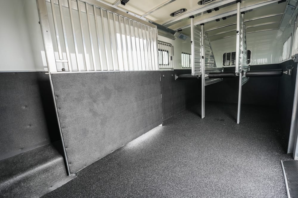 Interior of a horse trailer with metal partitions, padded walls, and a non-slip rubber floor for stalls