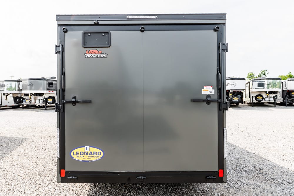 Rear view of a gray dual-door trailer in a lot, with black latches and a Leonard Truck Trailer sticker on the lower left side.