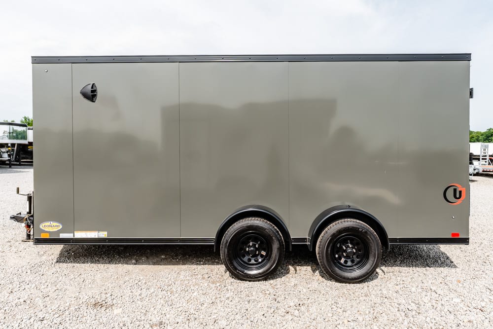 Side view of a gray enclosed dual-axle cargo trailer on a gravel lot.