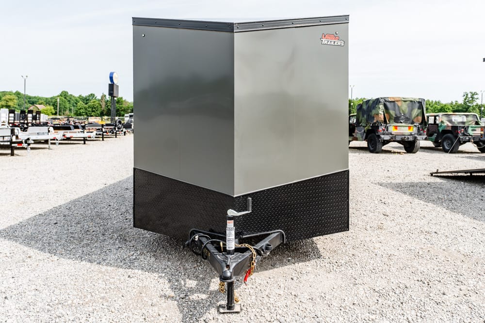 Enclosed gray cargo trailer with a black diamond-plate front, hitched and parked on a gravel lot.
