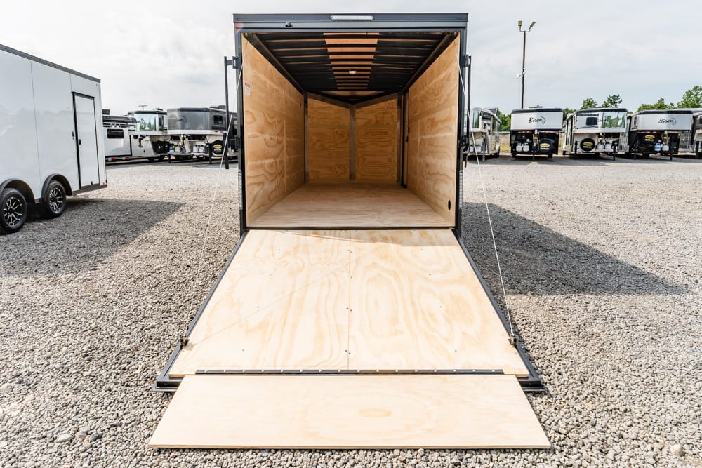 Open cargo trailer with ramp down, showing wooden interior for loading in a gravel lot of trailers