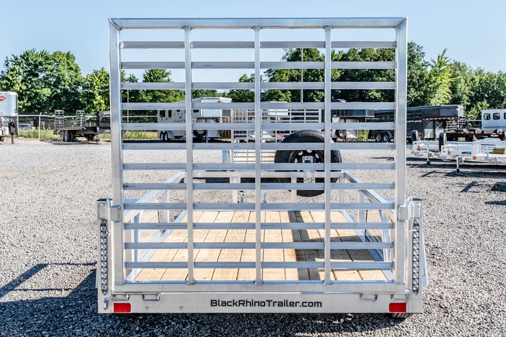 Rear view of a silver metal trailer with vertical bars, wooden deck, and a spare tire visible inside the frame.