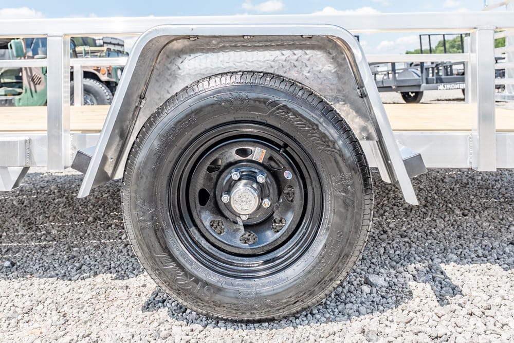 Trailer wheel with black steel rim and tire, metal fender, on gravel surface at a trailer lot