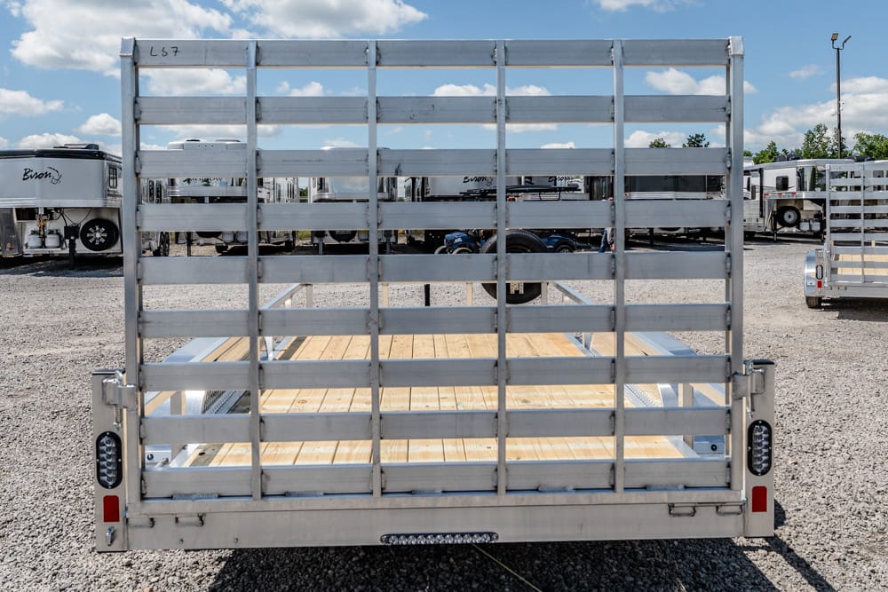 Rear view of a metal-framed utility trailer with a wooden floor, parked in a gravel trailer yard.