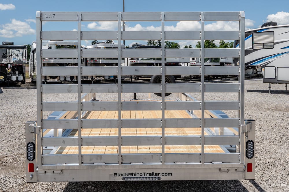 Rear view of a metal-framed utility trailer with a wooden deck, parked on gravel among RVs; BlackRhinoTrailer.com is visible on the bumper.