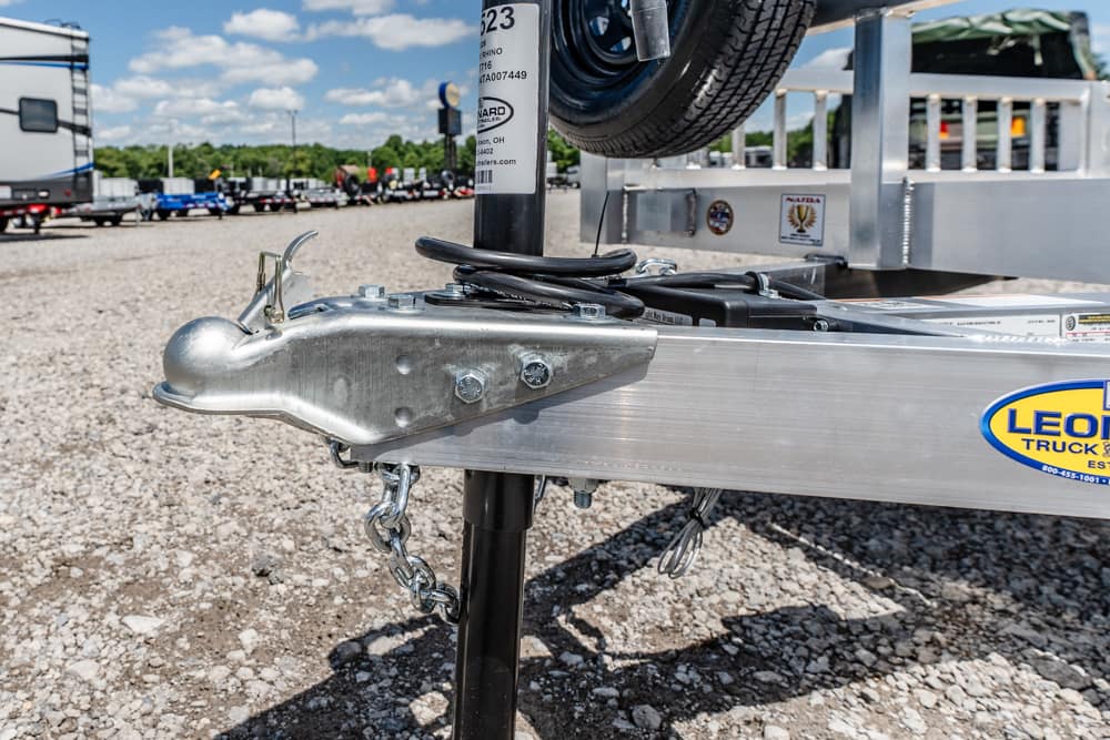 Close-up of a metal trailer hitch and jack on a silver aluminum trailer, with a coiled cable and a 'Leo' sticker visible in the foreground.