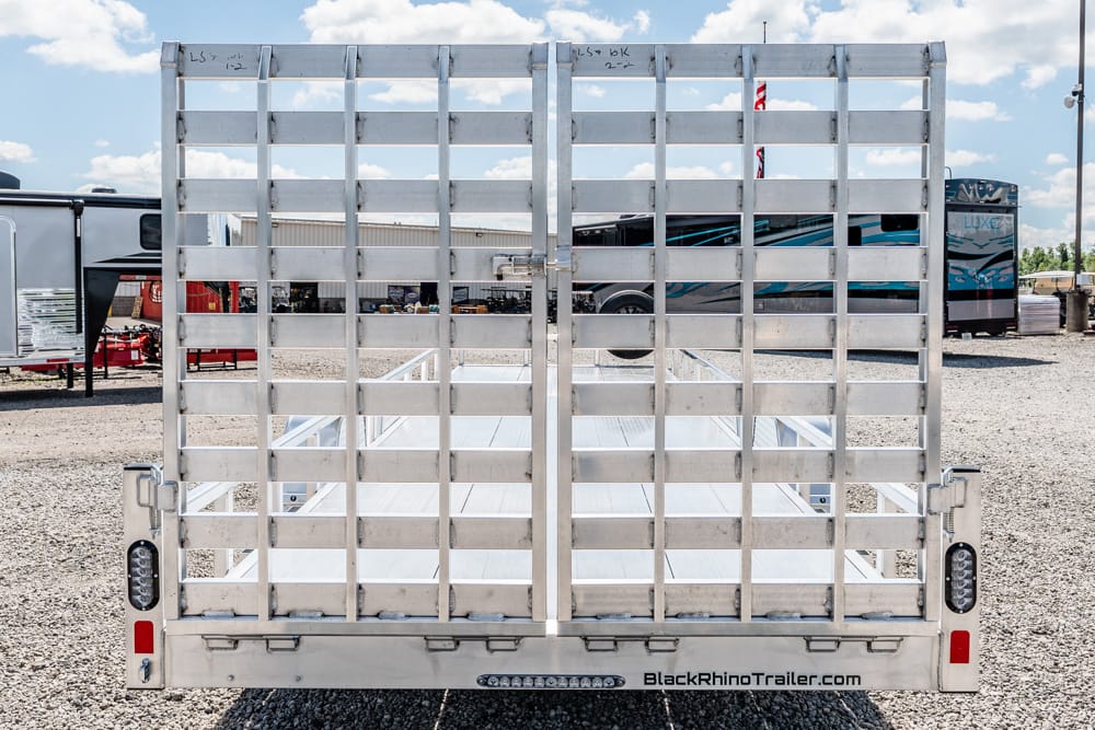 Rear view of a silver aluminum utility trailer with a slatted ramp gate on a gravel lot, brand BlackRhinoTrailer.com visible at the bottom edge.