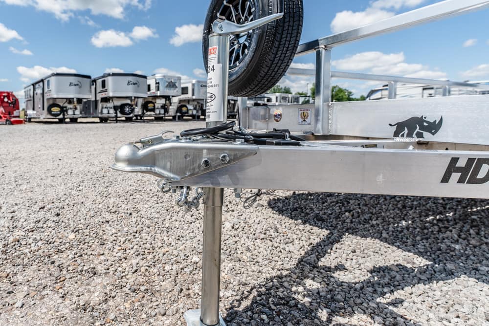 Close-up of a metal boat trailer hitch and jockey wheel on a gravel lot, with travel trailers in the background on a sunny day.
