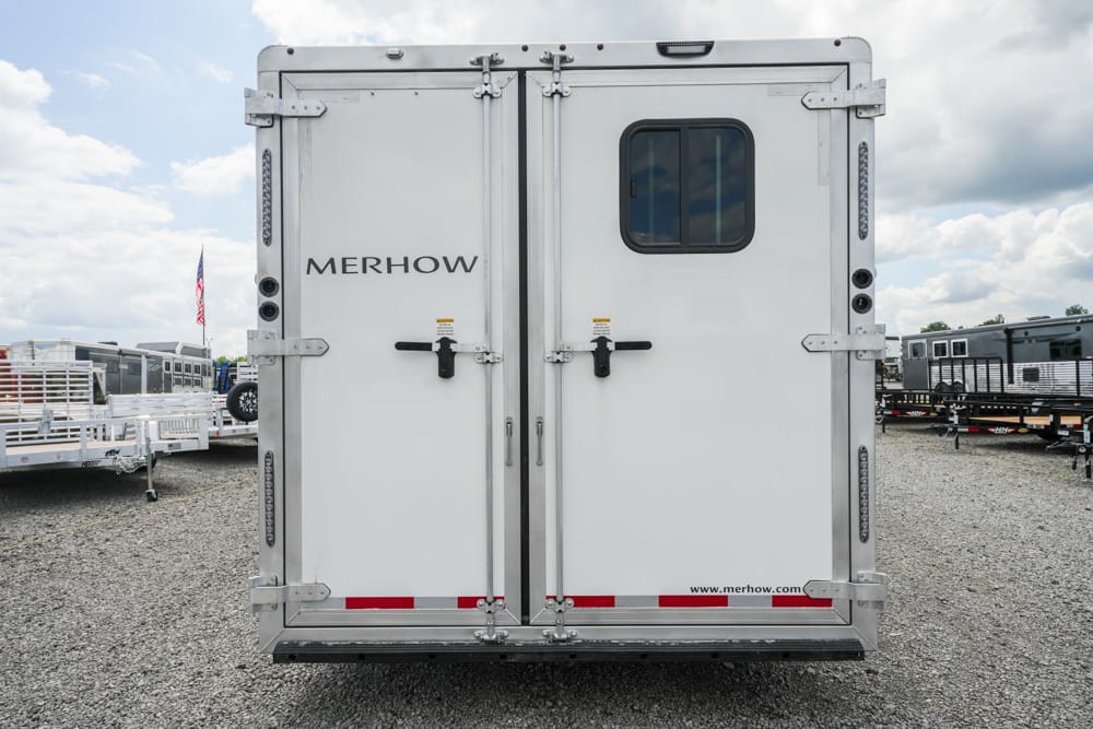 Rear view of a white Merhow horse trailer with double doors, small window, and gravel lot setting