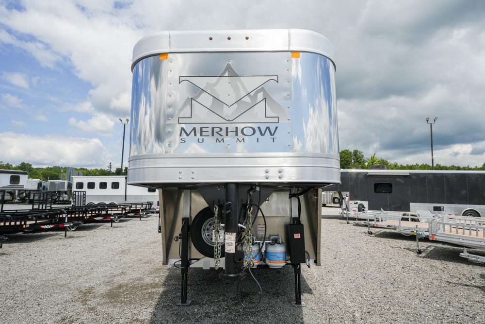 Front view of a shiny Merhow Summit horse trailer in a gravel lot with other trailers nearby.