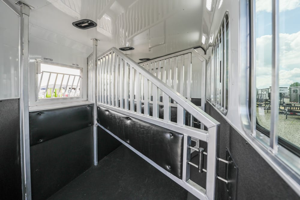 Interior of a white horse trailer with a metal divider and black padded wall, ready to transport a horse.