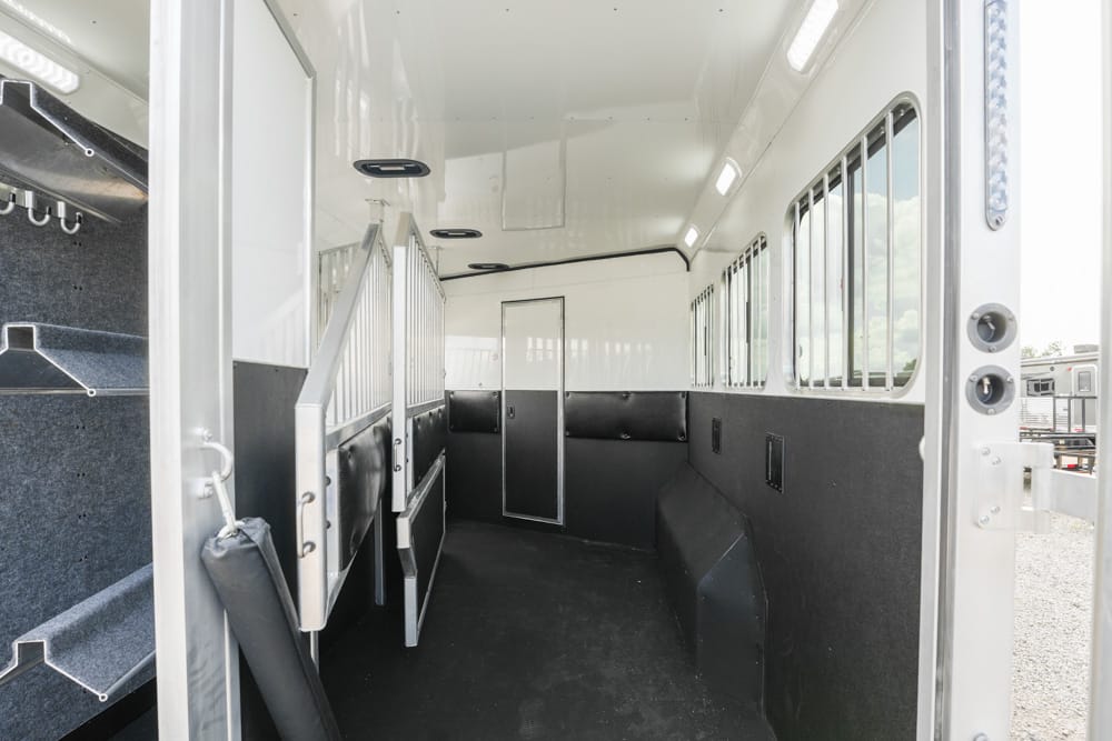 Interior of a white horse trailer with individual stalls, padded walls, and a door at the far end.