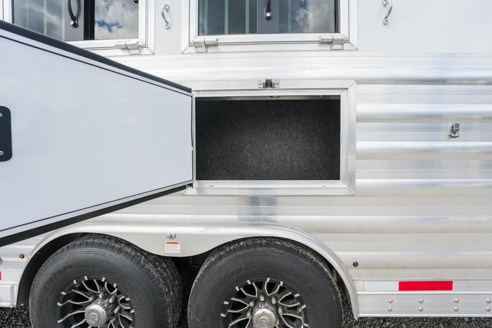 Open storage compartment on a silver travel trailer, revealing a dark, empty interior behind the door.