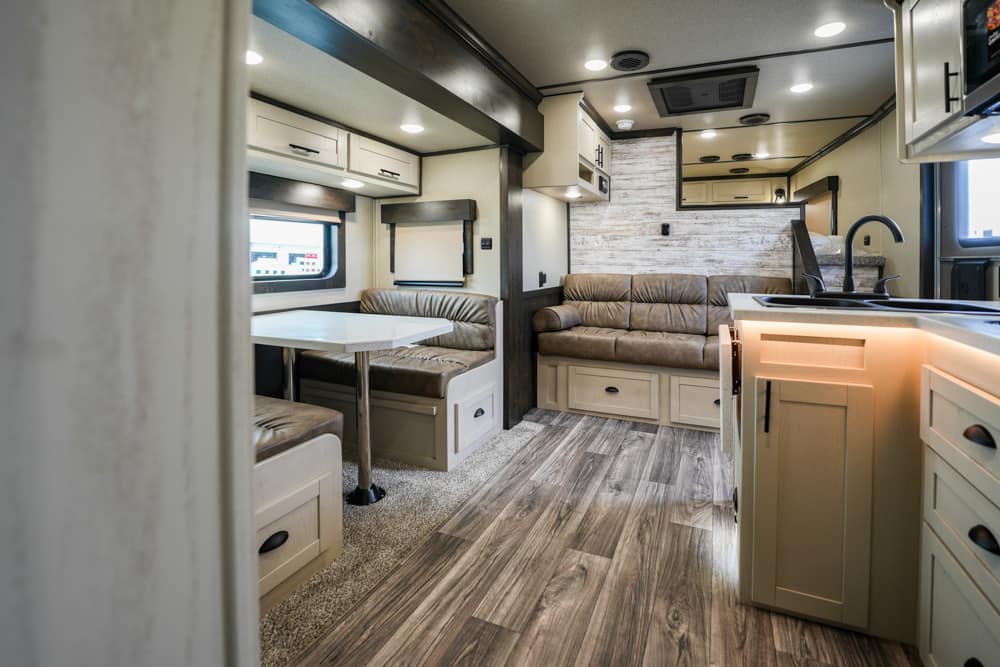 Interior of a modern RV: beige leather sofa, dinette, overhead cabinets, and a compact kitchen with sink.