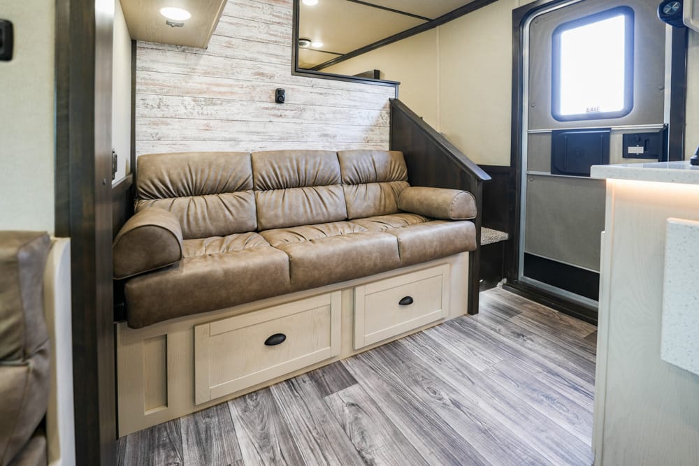 Cozy RV living area with a brown leather sofa and built-in storage drawers beneath, next to a small staircase and kitchen counter.