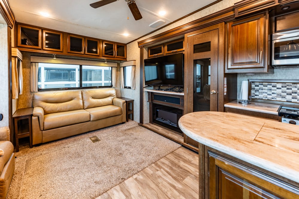 Cozy RV living area with a tan leather sofa, wood cabinets, and an entertainment center with TV and fireplace.