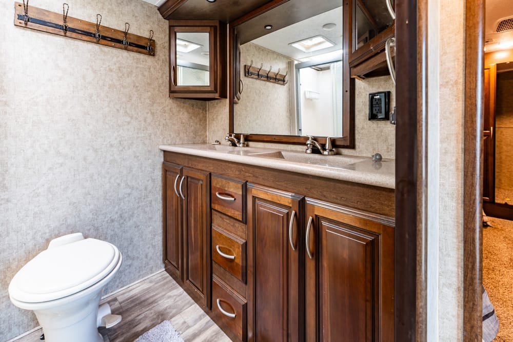 RV bathroom vanity with dual sinks, dark wood cabinets, and a large mirror above the countertop.