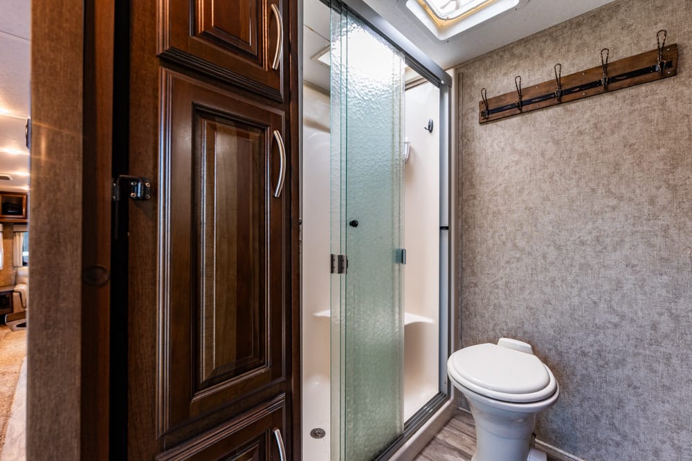 Compact RV bathroom with a glass shower door, wooden cabinet, and a white toilet.