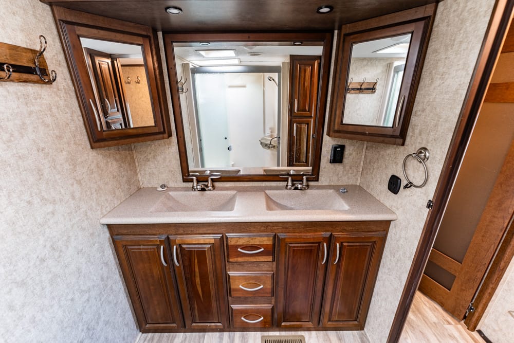 RV bathroom vanity with double sinks, dark wood cabinets, and a large mirror across the top.