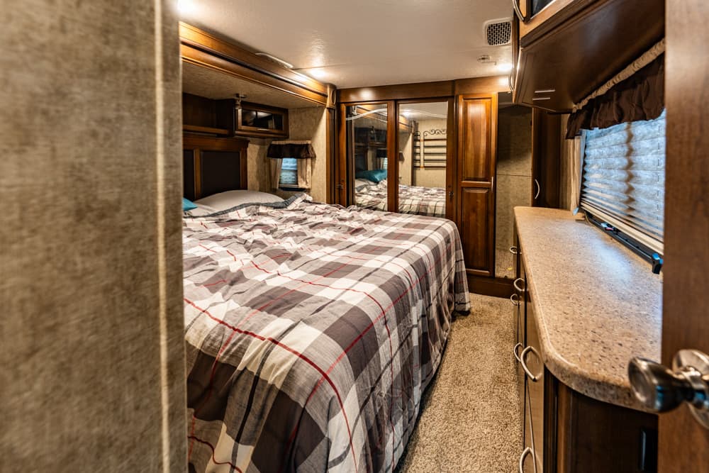 Cozy RV bedroom with a full bed, plaid comforter, and wood cabinets along the walls.
