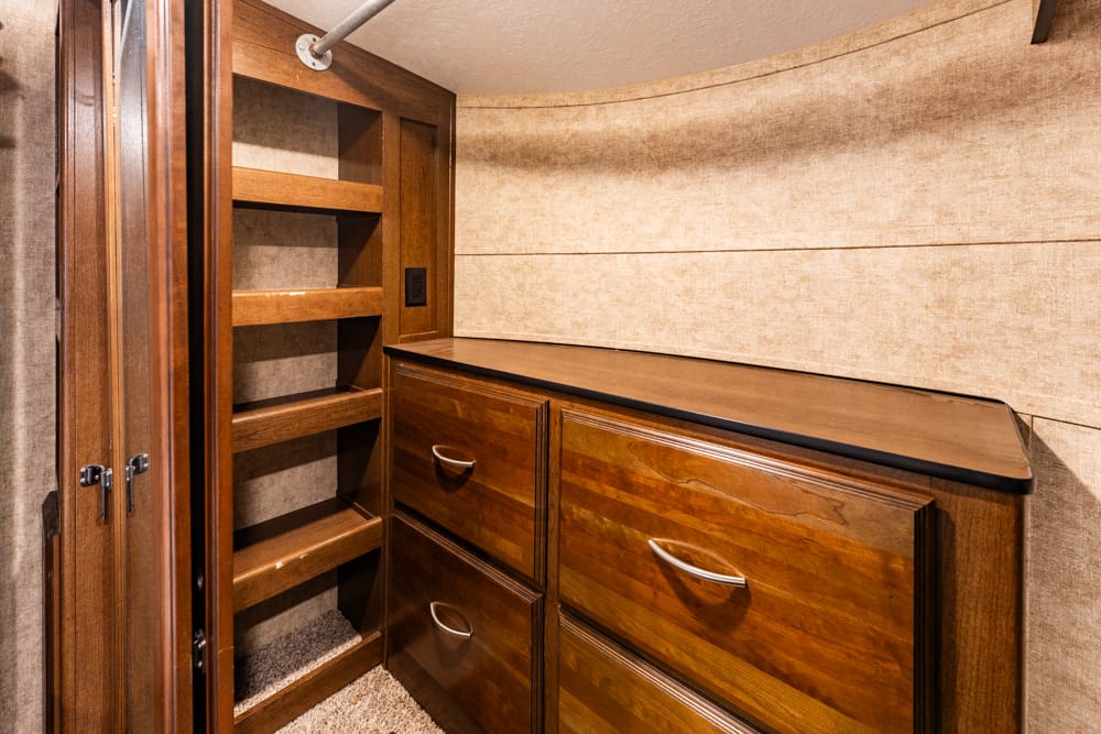 Tall wooden storage cabinet with four drawers and open-shelved pantry, in a beige-walled, compact RV or boat interior.