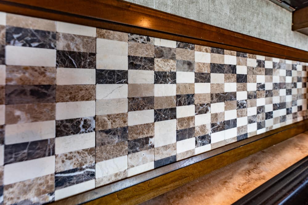 Checkerboard wall made of small square marble tiles in beige, brown, black, and white, framed by wooden trim.
