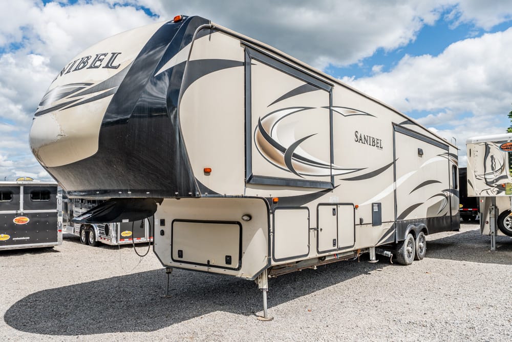 Beige and gray fifth-wheel RV with abstract swoosh graphics, parked on a gravel lot.