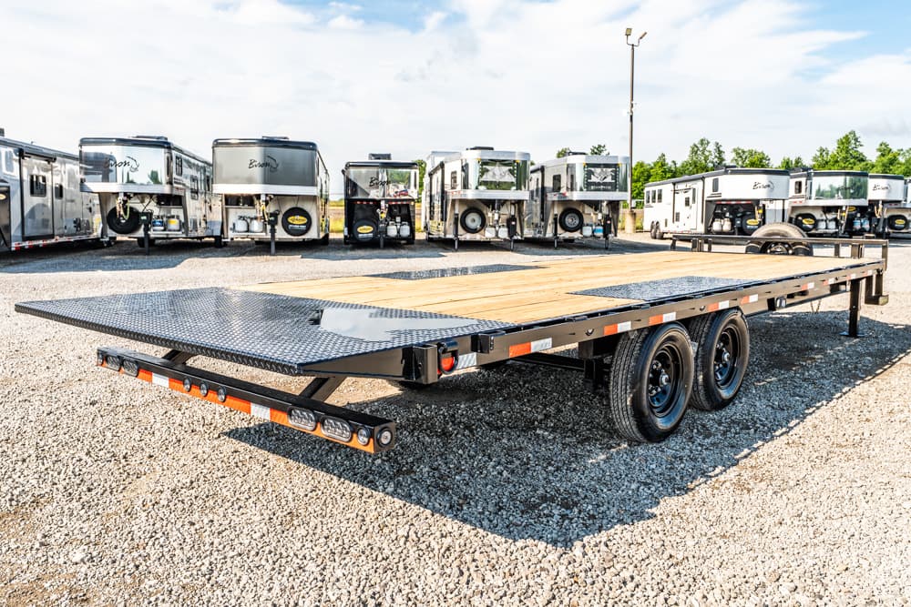 Flatbed trailer with wooden deck and dual axles parked in a gravel lot, rows of other trailers in the background